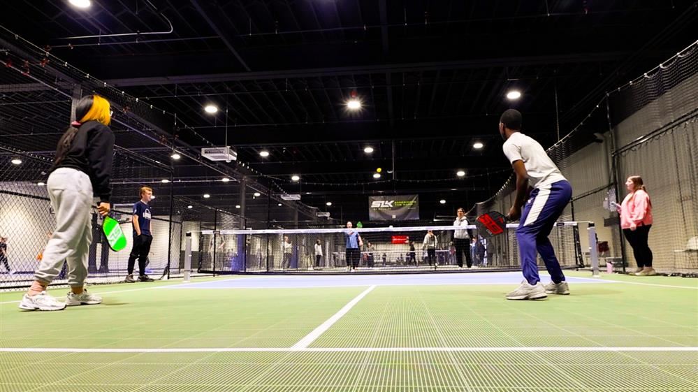  Four students are actively playing a match of pickleball.